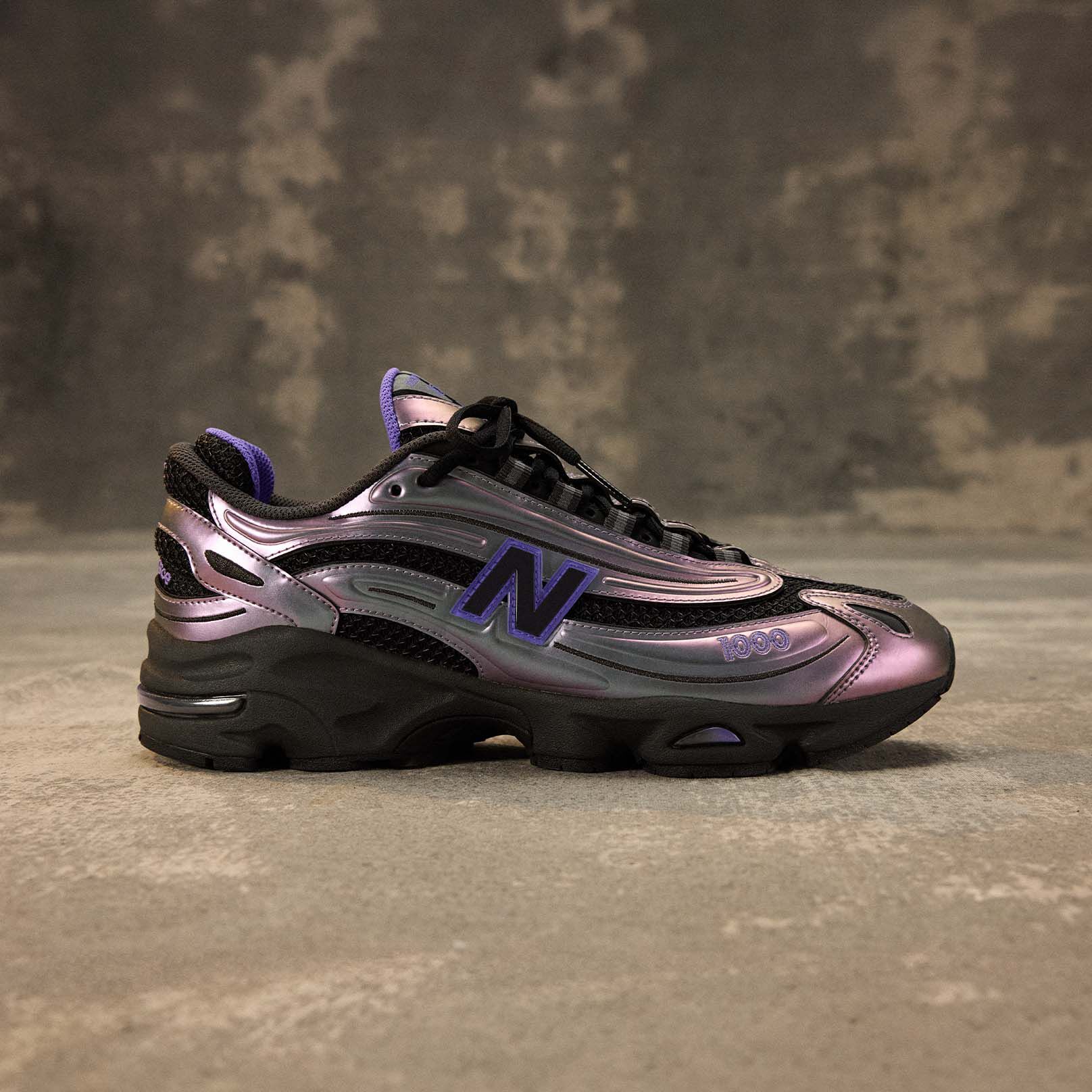 The 1000 New Balance shoe shot from the side behind a brown studio backdrop. 